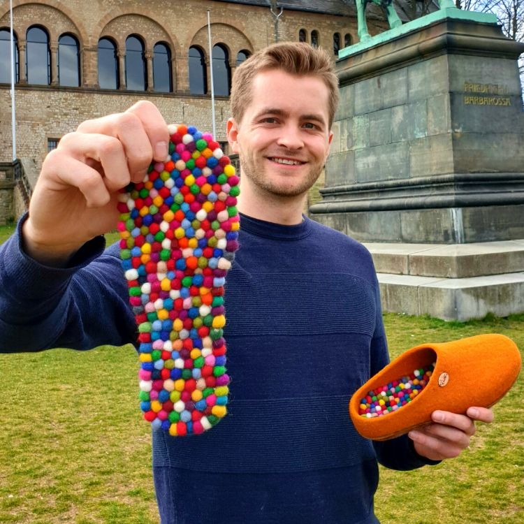 Person holding a colorful WoolFit FeelGood footbed beside an orange felt slipper